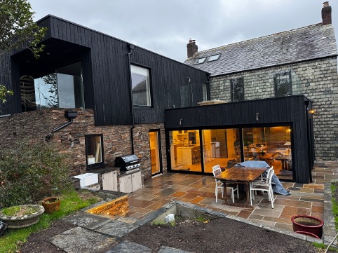 Evening view of the black timber extension and stone farmhouse at Mays Cottage