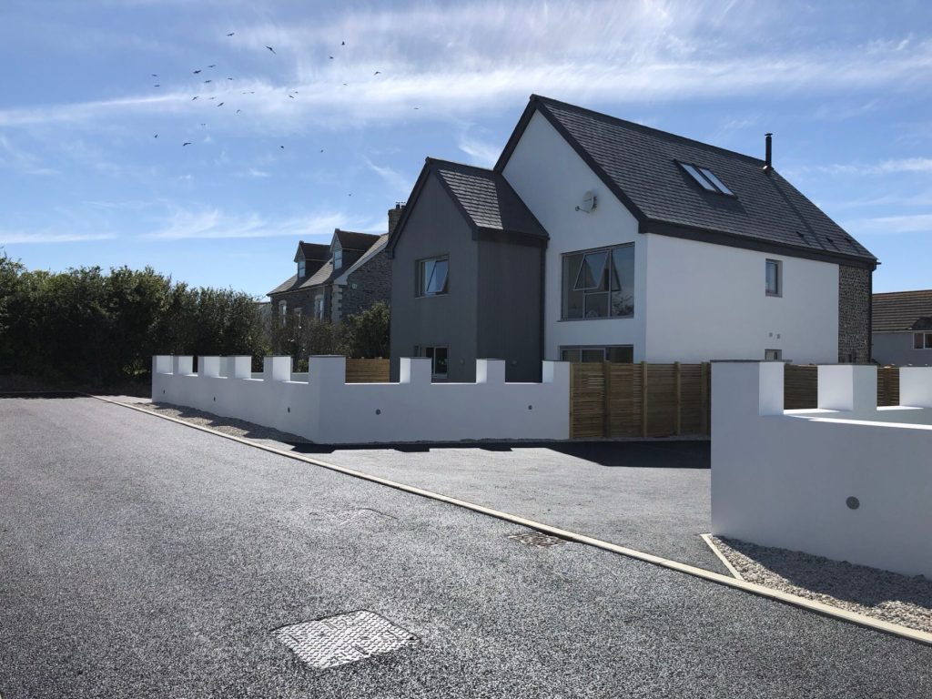 White rendered new homes and a crenellated boundary wall at The Meadows, St Merryn