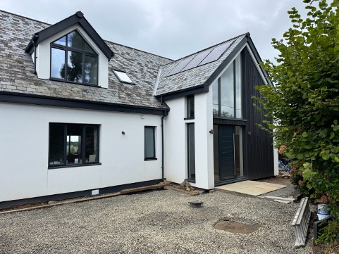 Side of the Tywardreath house, with solar panels, a slate roof and a glazed entrance